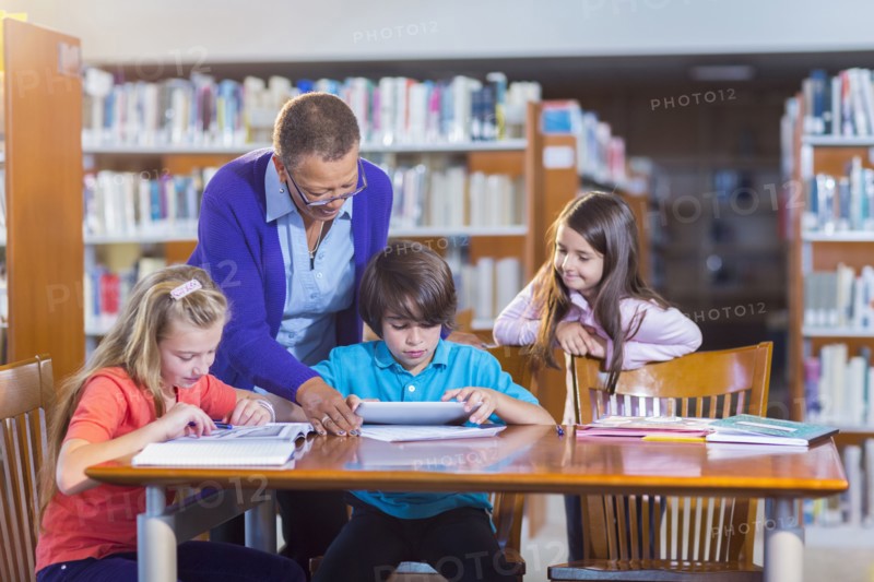Teacher helping student use digital tablet in library