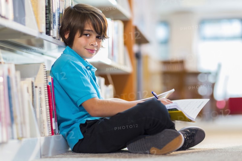 Mixed race student writing in notepad on floor in library
