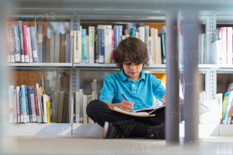 Mixed race student writing in notebook on floor in library
