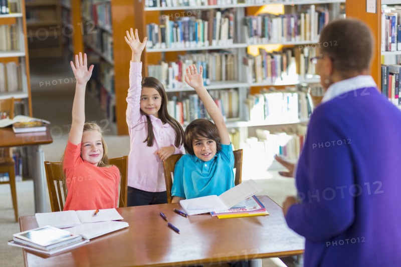 Students raising their hands in library