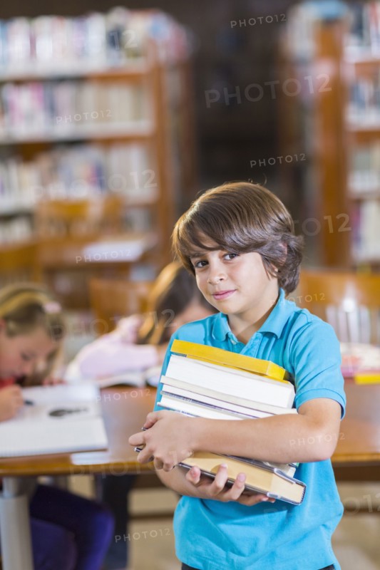 Student carrying stack of books in library