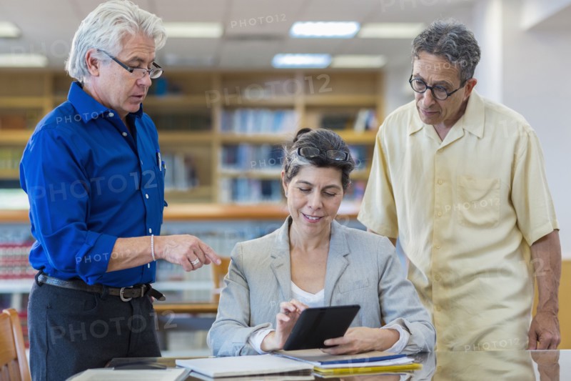 Teacher helping adult students use digital tablet in library
