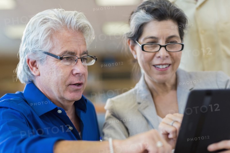 Hispanic teacher helping adult student use digital tablet