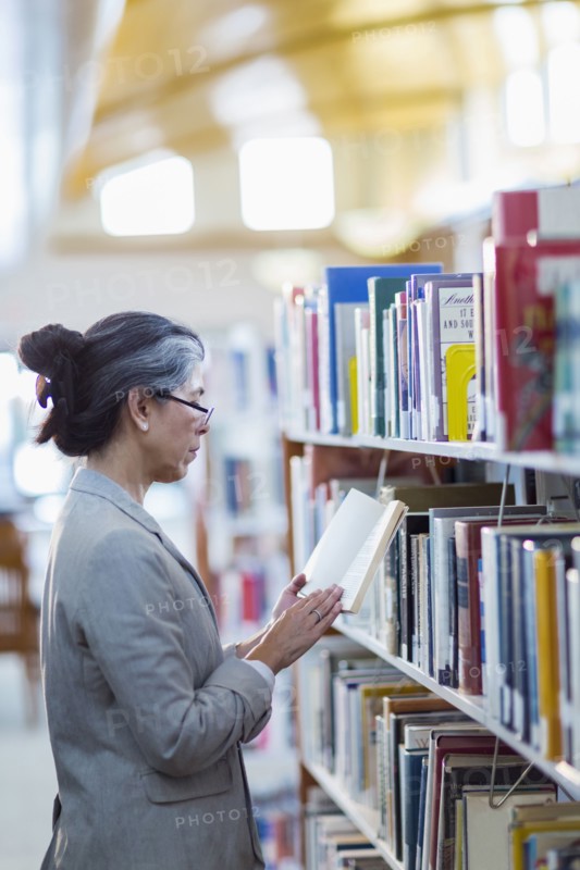 Older Hispanic woman reading book in library