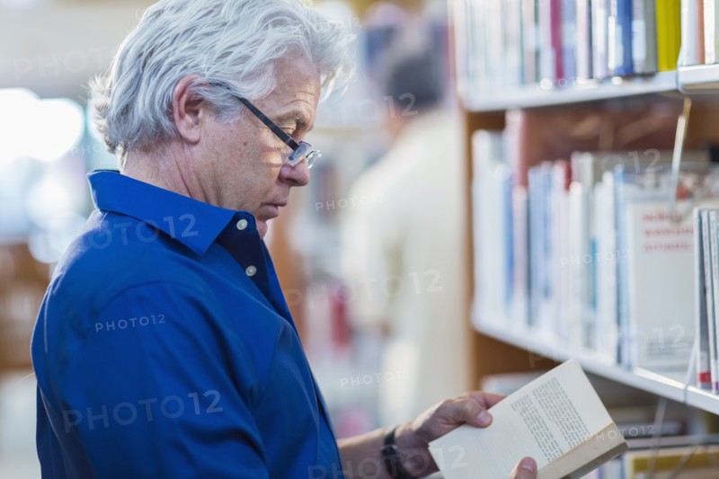 Older Hispanic man reading book in library