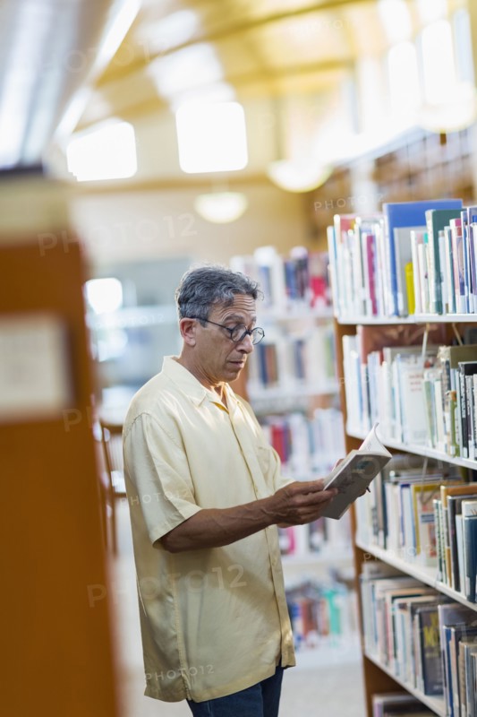 Older Caucasian man reading book in library