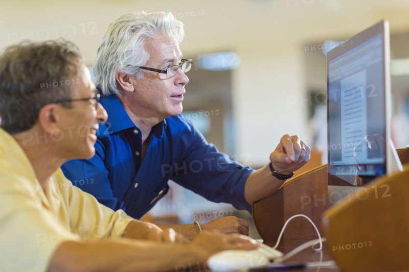 Teacher helping adult student use computer in library