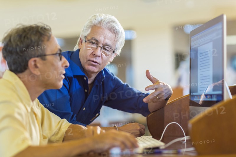Teacher helping adult student use computer in library