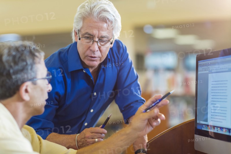 Teacher helping adult student use computer in library