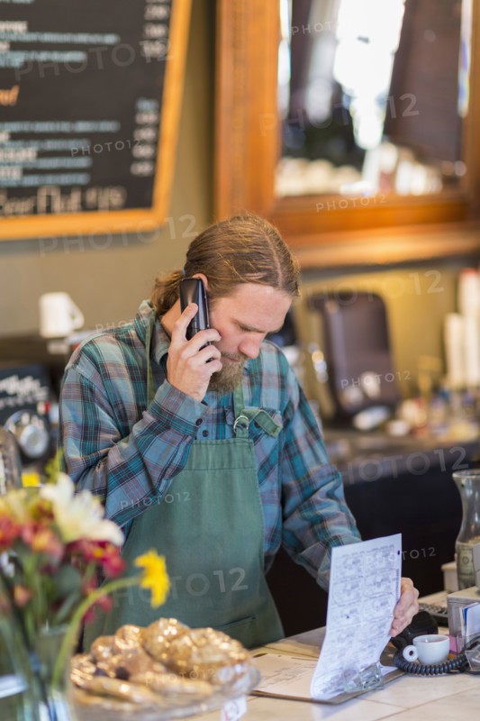 Caucasian server on telephone reading clipboard in cafe