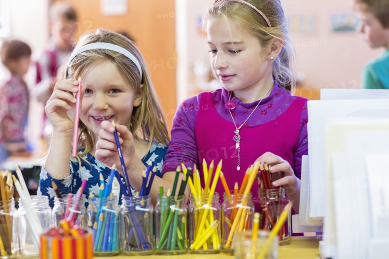 Caucasian girls choosing multicolor pencils in classroom