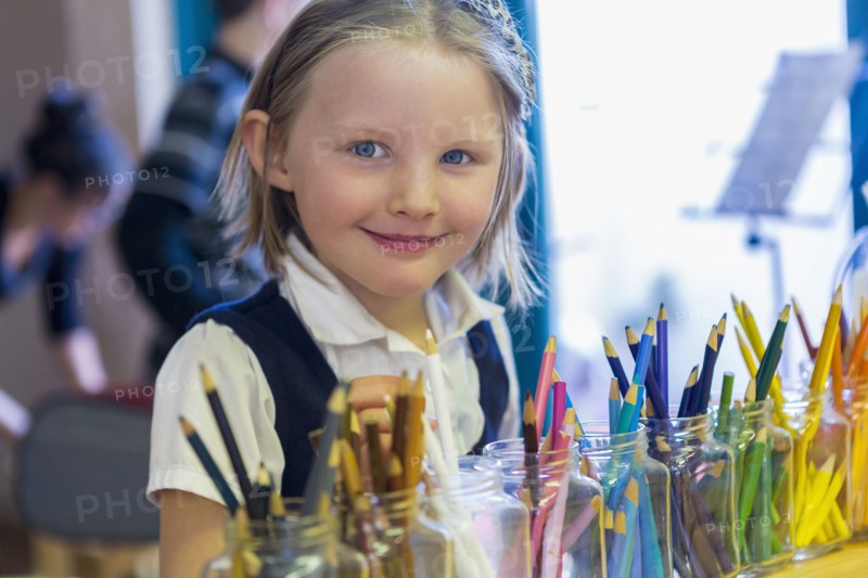 Mixed race girl smiling near multicolor pencils in classroom