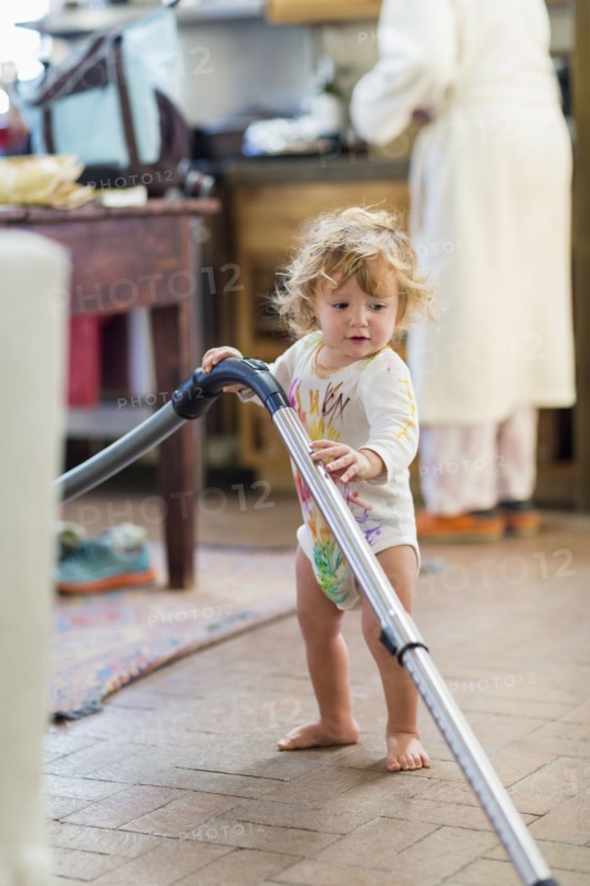 Caucasian baby boy vacuuming in kitchen