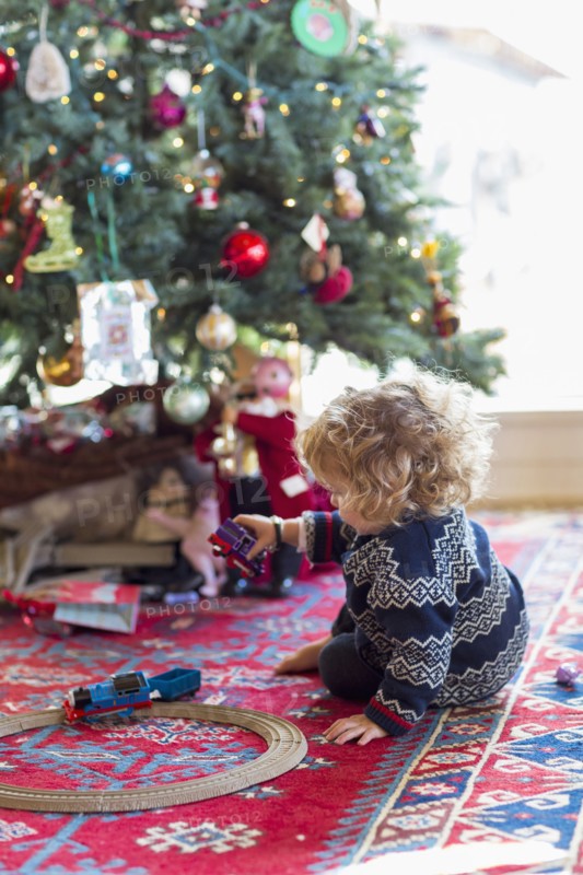 Caucasian baby boy playing with toys under Christmas tree