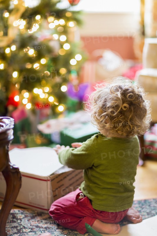 Caucasian baby boy opening presents near Christmas tree