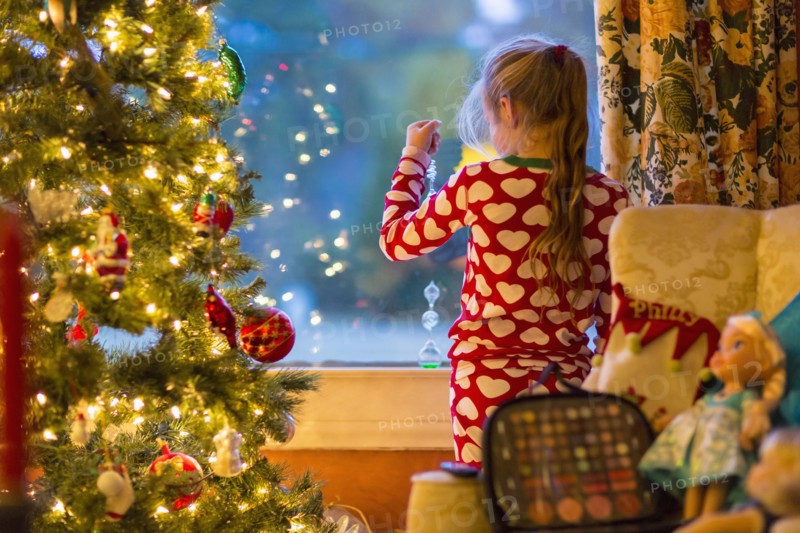 Caucasian girl looking out window near Christmas tree