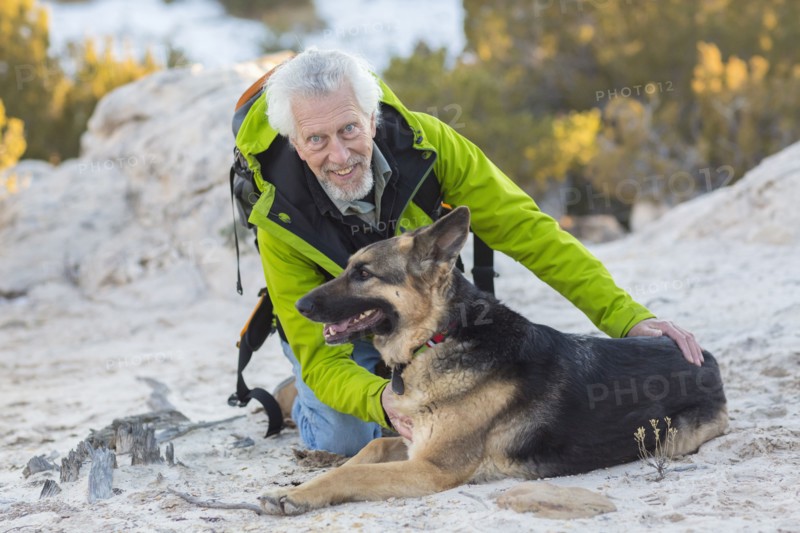 Older man petting dog on rocky hillside
