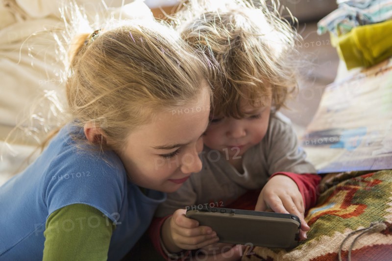 Caucasian brother and sister using cell phone on sofa