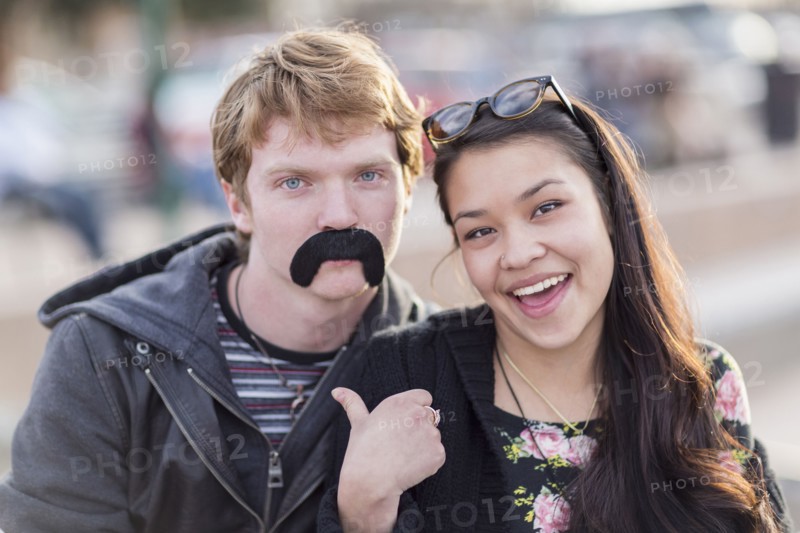 Teenage couple playing with fake mustache