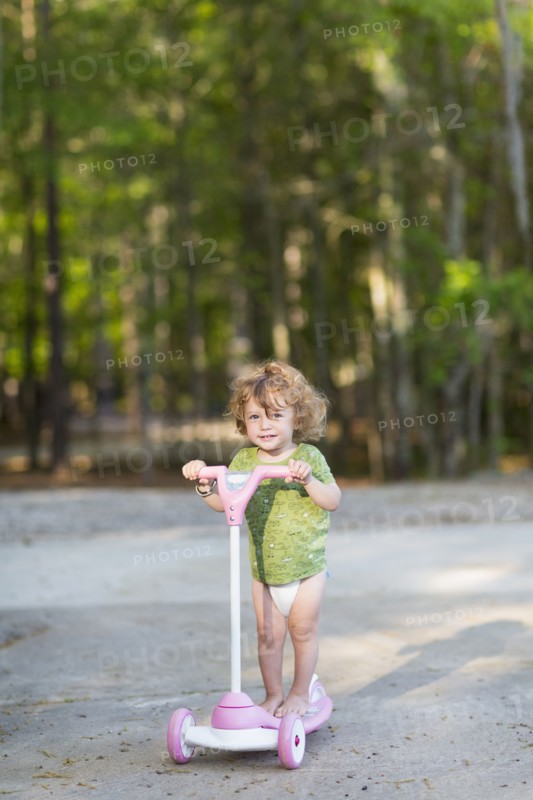 Caucasian baby boy riding scooter on dirt path