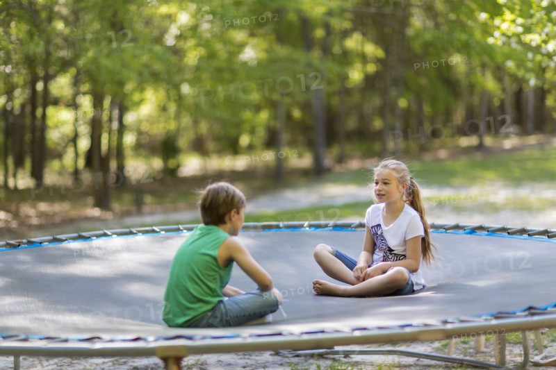 Caucasian children sitting on trampoline