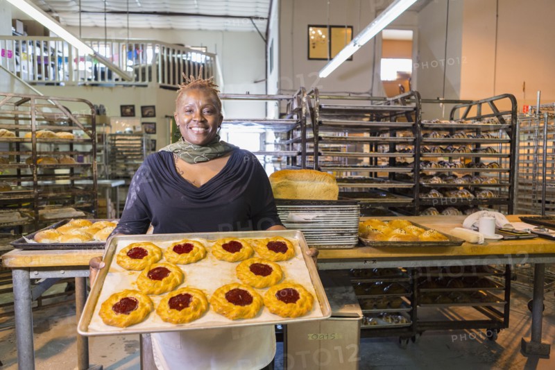Black baker holding tray of pastries in bakery kitchen