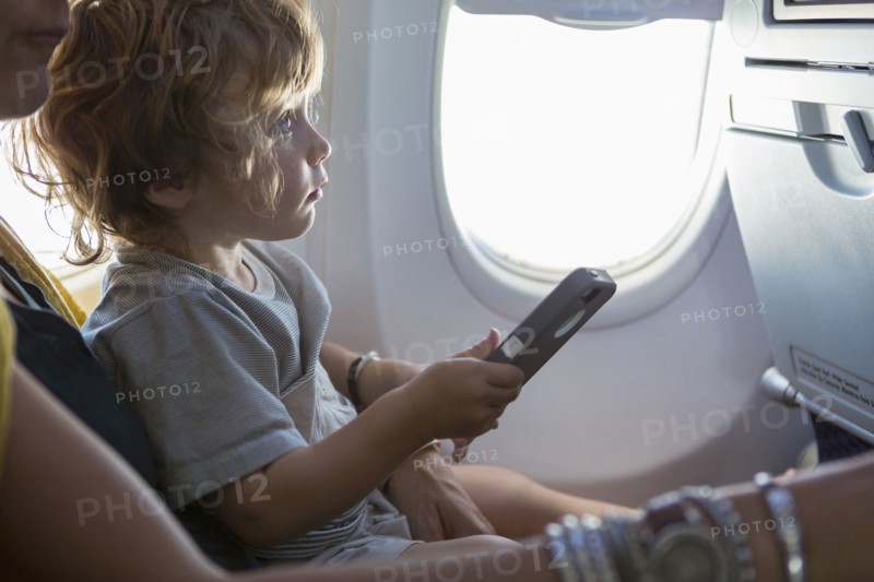 Caucasian mother and baby son using cell phone on airplane