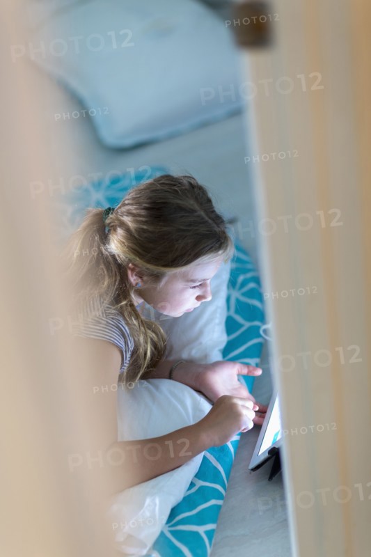 Caucasian girl using digital tablet on bed at night