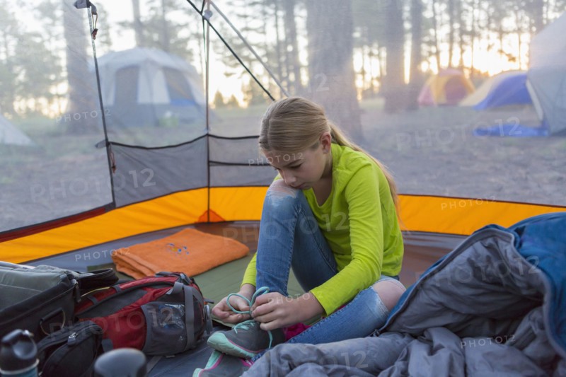 Caucasian girl tying shoes in camping tent