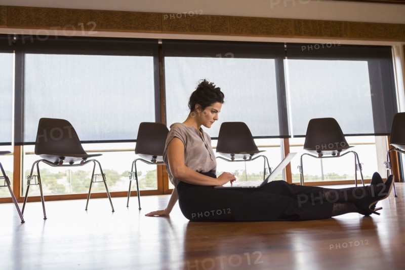 Mixed race businesswoman using laptop on floor of meeting room
