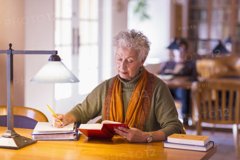 Older mixed race woman reading book in library