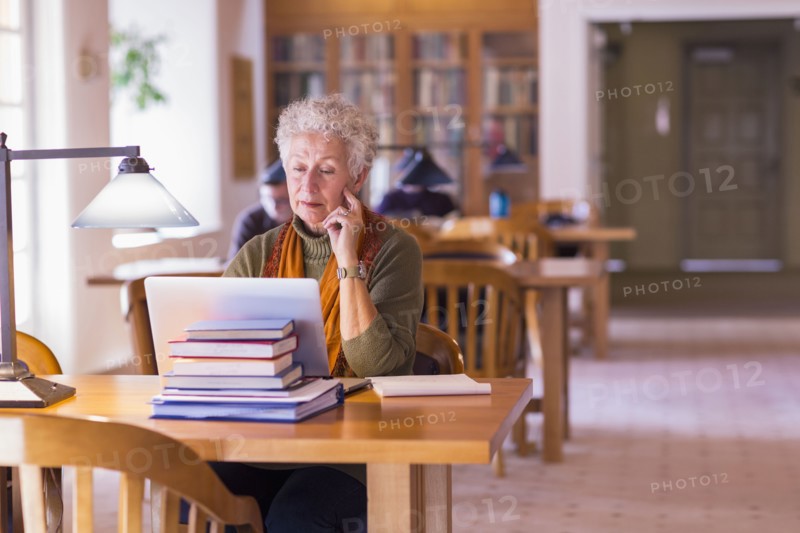 Older mixed race woman using laptop in library