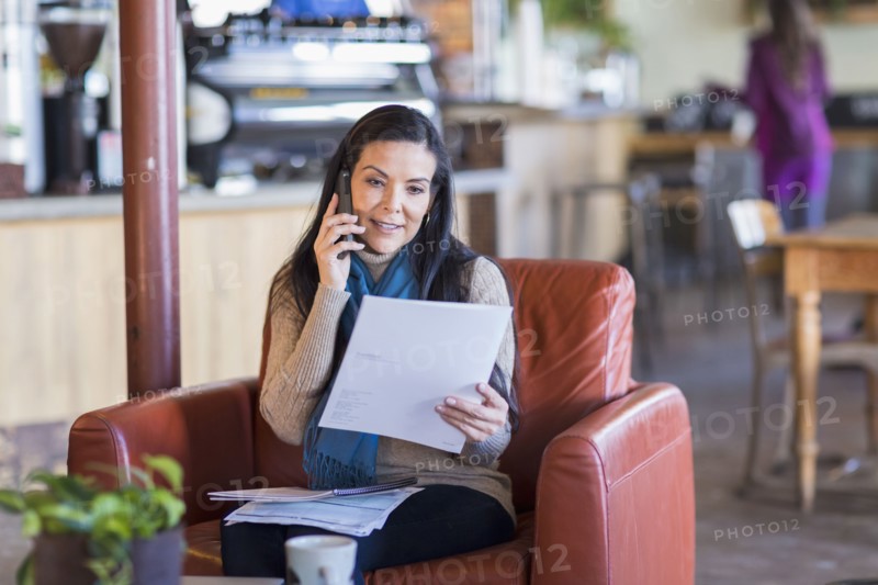 Hispanic woman paying bills on cell phone in cafe