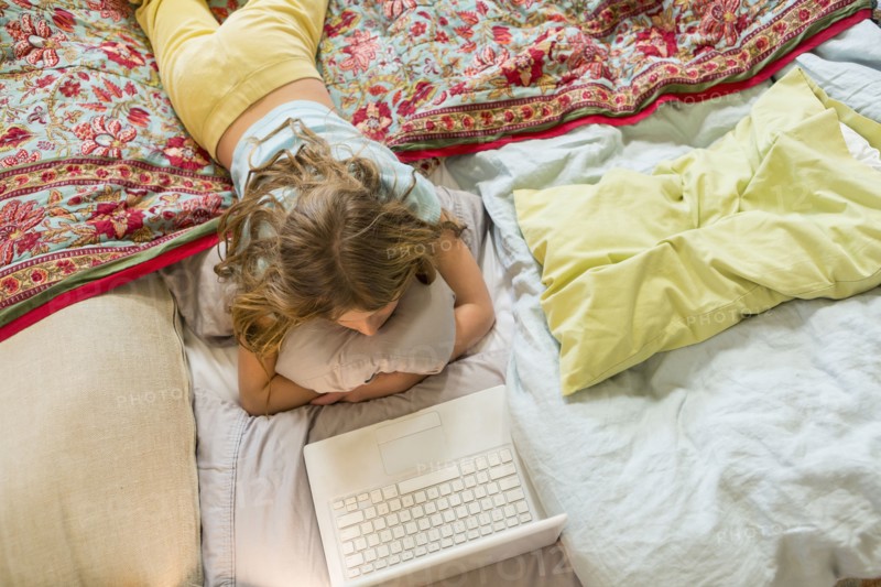 Caucasian girl using laptop on bed