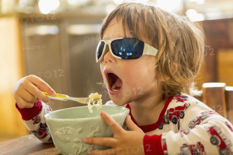 Caucasian boy in sunglasses eating in kitchen
