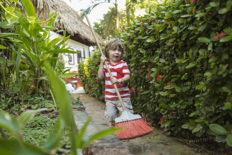 Caucasian boy playing with broom on path near house