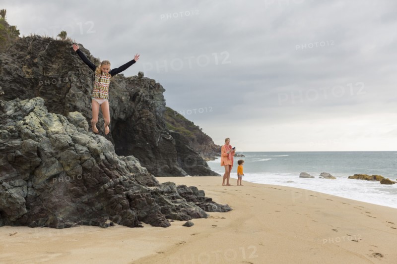 Caucasian girl jumping off rocks at beach