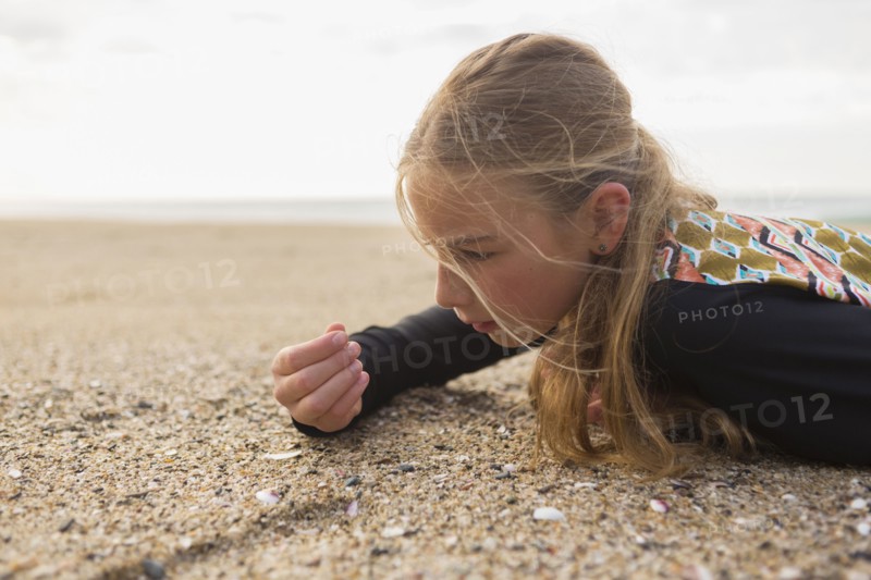 Caucasian girl laying on beach examining seashells