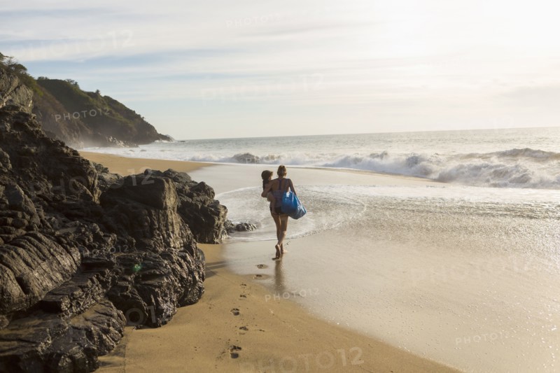 Caucasian mother carrying son on beach