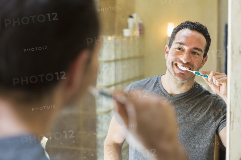 Hispanic man brushing teeth in mirror