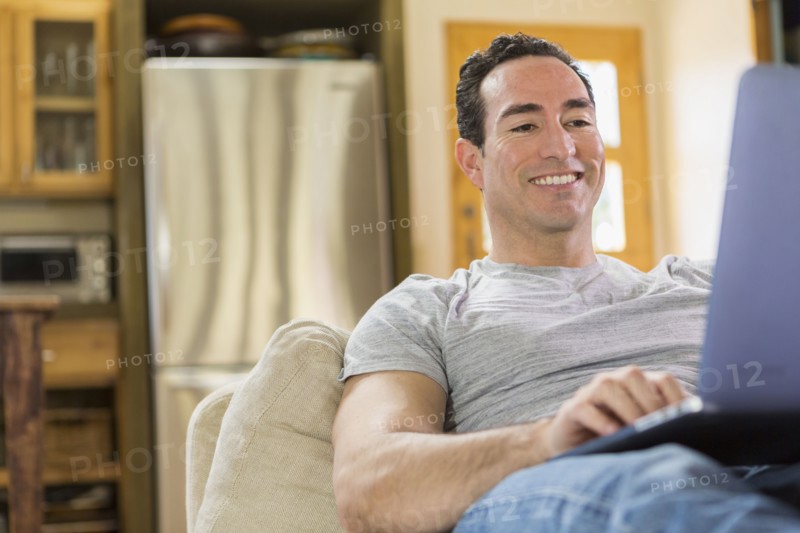 Hispanic man laying on sofa using laptop