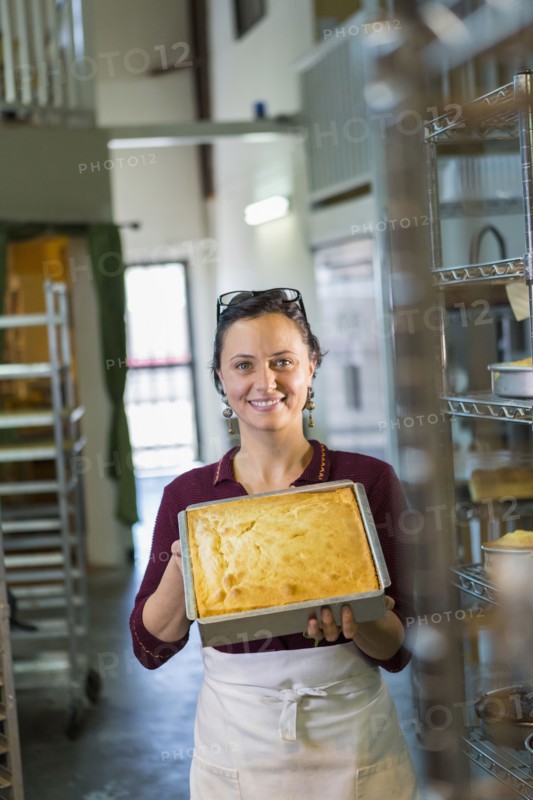 Caucasian woman showing cake in bakery pan