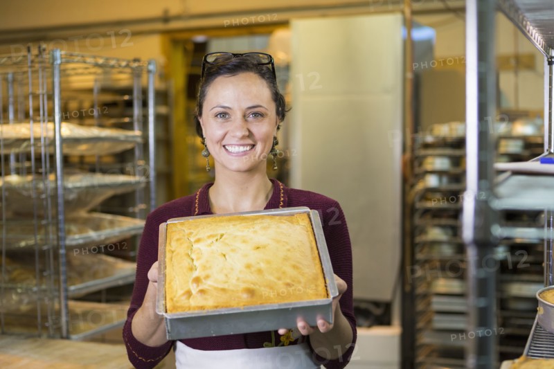 Caucasian woman showing cake in bakery pan
