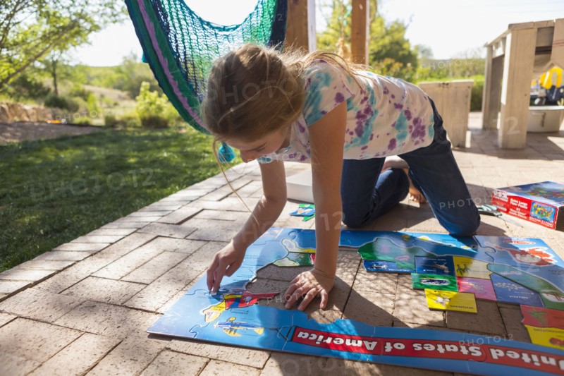 Caucasian girl kneeling on patio assembling puzzle