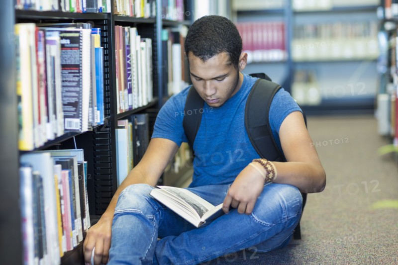 Mixed Race boy sitting on floor reading book in library