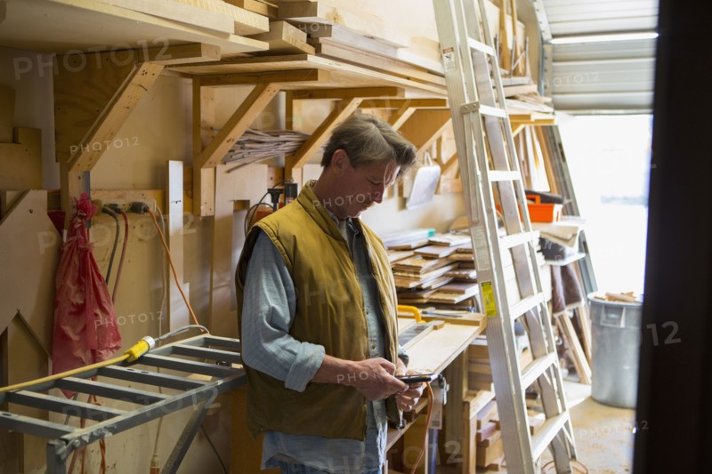 Caucasian carpenter texting on cell phone in workshop