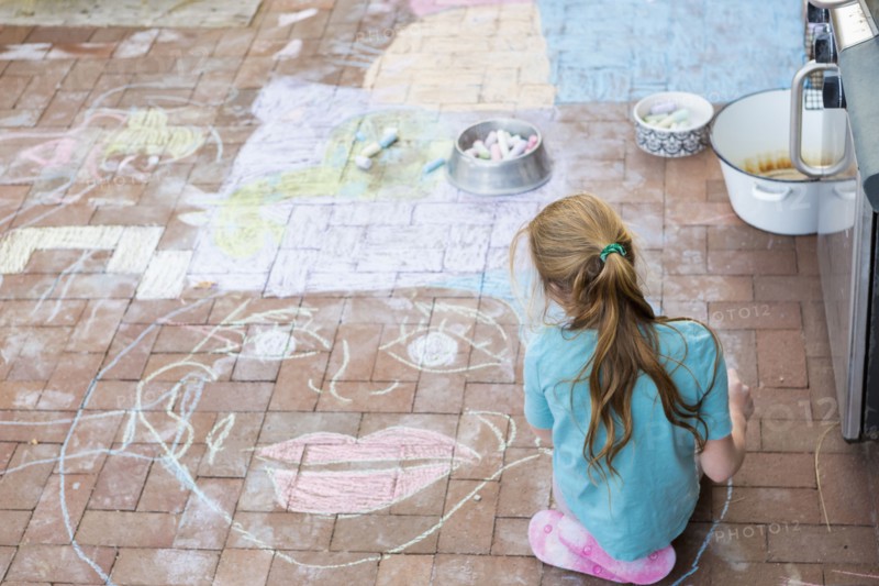 Caucasian girl drawing face with chalk on patio bricks