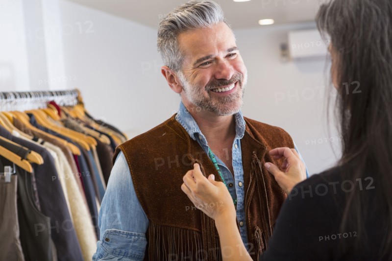 Woman helping man with fringe vest in store