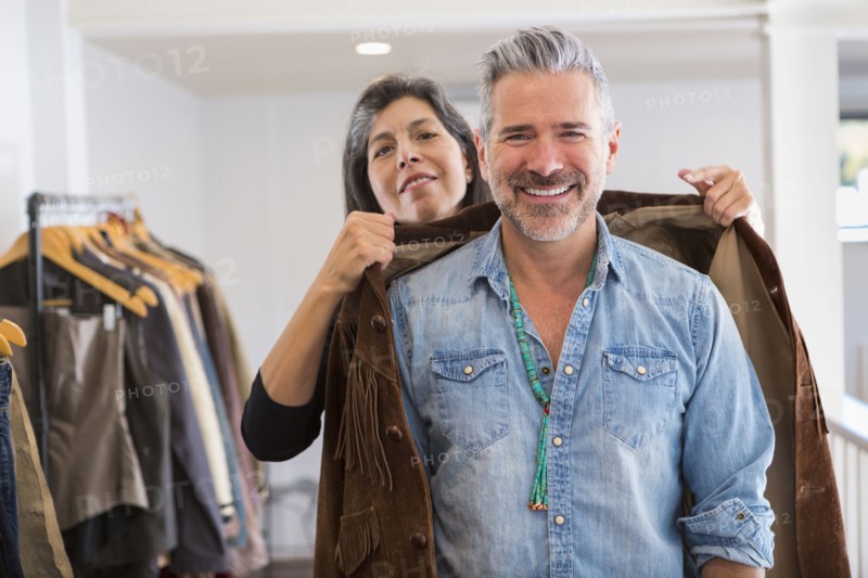 Woman helping man with fringe jacket in store