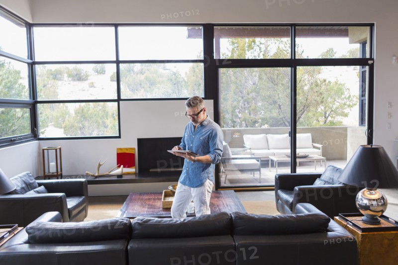 Caucasian man standing in livingroom using digital tablet